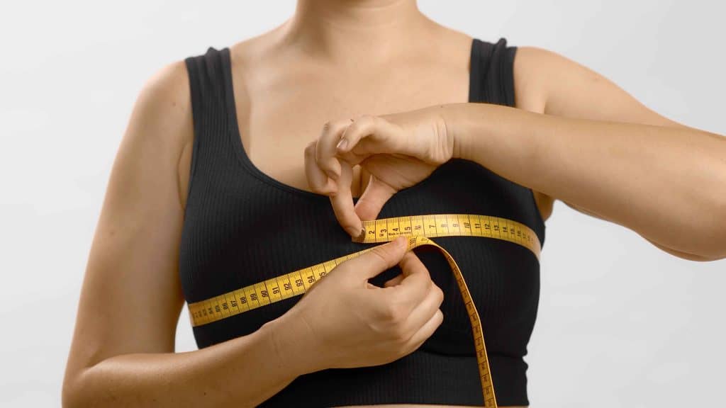 Accurate waist measurement with a yellow tape measure on a woman's black tank top.
