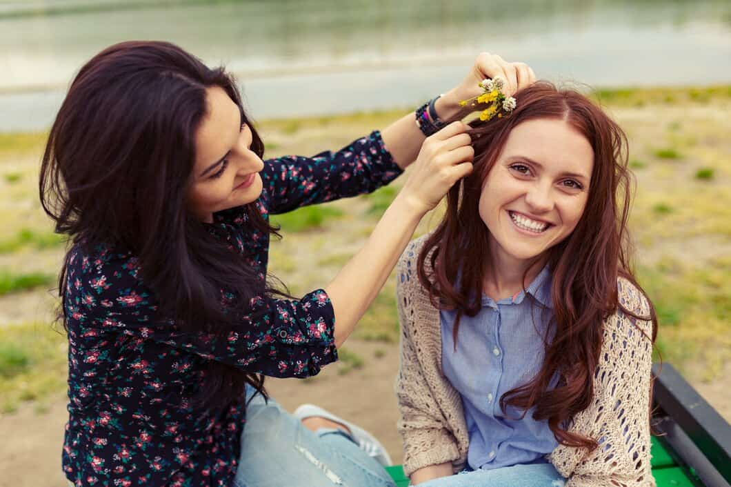 Woman smiling as friend places flower crown on her head outdoors.